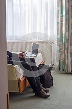 Adult male in service interest who reads news on the phone and laptop inside the hotel room