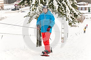 Adult male snowboarder using ski drag rope lift to rise up to the slope top at ski resort