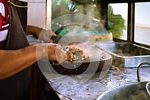 Adult male taquero cutting meat at a Mexican restaurant to prepare carnitas tacos.