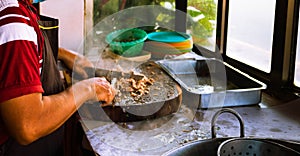 Adult male taquero cutting meat at a Mexican restaurant to prepare carnitas tacos.