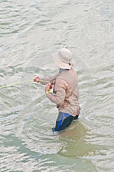 Adult male, wading in tropical water, hauling a gill net, filled with bait fish