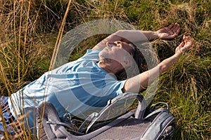 An adult man with a backpack rests in the tall grass after a long walk