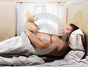 Adult man in bed looks at toy bear