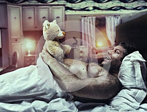 Adult man in bed looks at toy bear