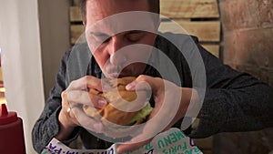 Adult man is biting juicy hamburger in cafe, close-up view