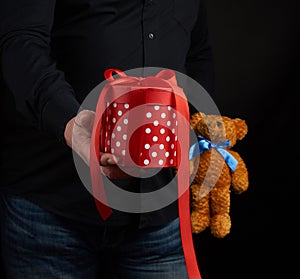 Adult man in a black shirt holds a blue square box tied with a red ribbon