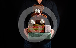 Adult man in a black shirt holds a blue square box tied with a red ribbon and brown teddy bear