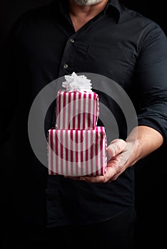 Adult man in a black shirt holds in his hand a stack of paper-wrapped gifts