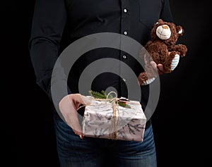 Adult man in a black shirt holds a square box and brown teddy bear