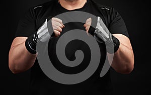 Adult man in a black uniform and muscular arms stands in a sports stance, holds a sports elastic bandage