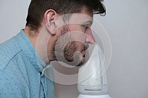 An adult man breathes steam, treats the airways with a nebulizer at home.