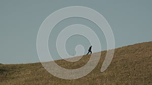An adult man in a business suit walks to the top of the hill on the horizon against the blue sky