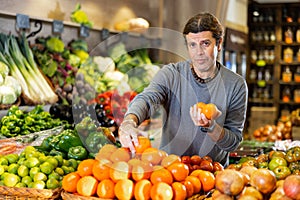 Adult man buyer chooses tangerines in shop