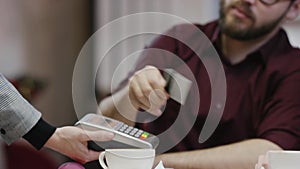 Adult man is calling a waiter and paying the bill with his credit card