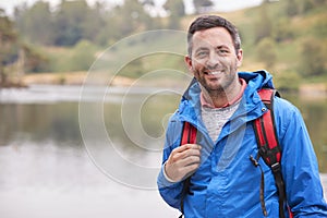 Adult man on a camping holiday standing by a lake smiling to camera, portrait, Lake District, UK