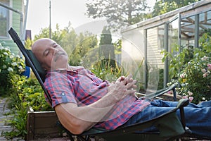 Adult man in casual clothing sitting in a deck chair and resting having a nap.