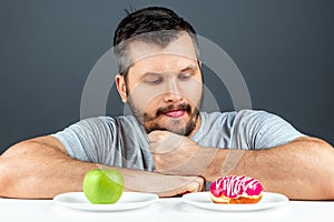 An adult man chooses between a donut and a green apple. Concept Resistance to temptation, fast food, healthy food, diet, body care