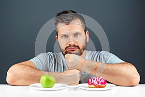 An adult man chooses between a donut and a green apple. Concept Resistance to temptation, fast food, healthy food, diet, body care