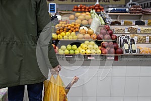 Adult man choosing buying fresh fruits at market and holding package with mutton meat. Food shopping concept