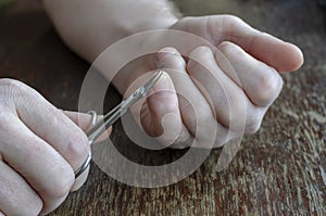 An adult man is cutting his hand nails with manicure scissors