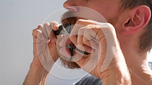 Adult man cutting his own beard and mustache with scissors and comb. Caucasian red bearded male trimming hair on face at home 4K