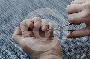 Adult man is cutting his own hand nails with manicure scissors