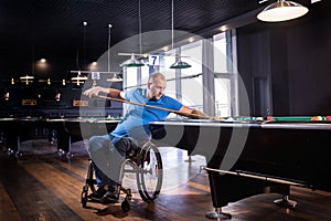 Adult man with disability in a wheelchair play billiards in the club