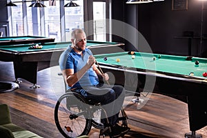 Adult man with disability in a wheelchair play billiards in the club