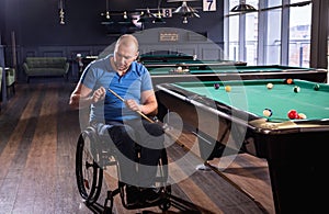 Adult man with disability in a wheelchair play billiards in the club