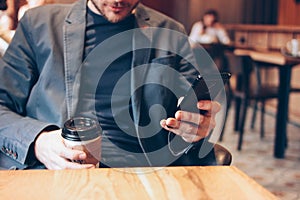 Adult man drinking coffee from paper cup and using mobile phone at cafe