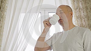 Adult man drinking morning coffee on cozy kitchen on window background. Portrait cheerful man enjoying hot tea from cup