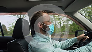 Adult man driving car wearing protective face mask during the coronavirus epidemic.