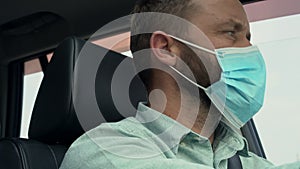 Adult man driving car wearing protective face mask during the coronavirus epidemic.