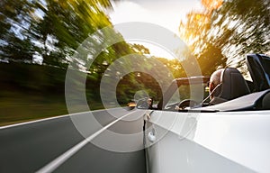 Adult man is driving with convertable car in sunny nature on a bright summer day. wide angle pursuit shot with high speed motion