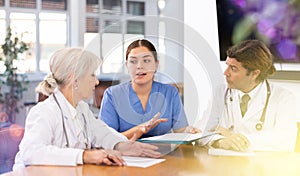 Adult man, elderly and young women doctors have meeting at table