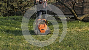 Adult man with electric lawnmower, lawn mowing. Gardener trimming a garden