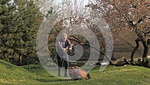 Adult man with electric lawnmower, lawn mowing. Gardener trimming a garden