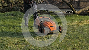 Adult man with electric lawnmower, lawn mowing. Gardener trimming a garden