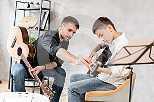 Adult man explains his son, who learn to play guitar, how to play studied chord correctly. Education with family