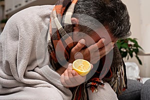 Man feeling unwell holding lemon covering eye with hand photo