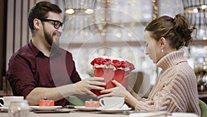 Adult man gives flowers he got from a waiter to his wife while sitting in restaurant and she kisses him