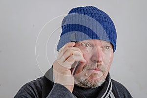 A adult man with gray stubble on his face is talking on his cell