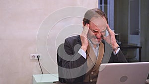 Adult man with headache while working on laptop in a modern office.