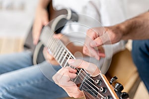 Adult man helps his little brother to learn how to play elecrtric guitar