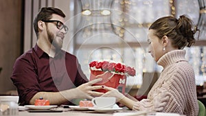 Adult man and his wife are sitting by table in restaurant and man calls waiter who brings flowers to them and man gives