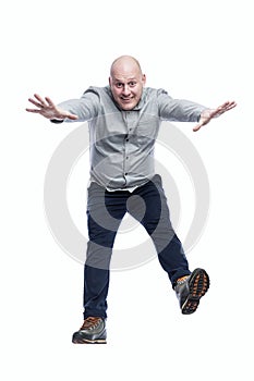 An adult man jumps funny. Red-haired bald guy in a gray shirt and trousers. Energy and emotions. Full height. Isolated on a white