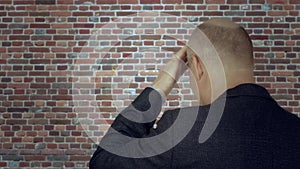 Adult man knocking hand on forehead back view on brick wall background