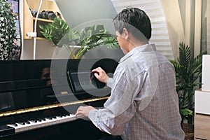 Adult man learning to play piano using digital tablet at home, Happy Asian businessman relaxing by playing piano, Reduce stress