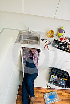 Adult Man Lying On Floor Repairing Sink In Kitchen