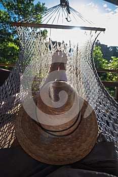 Adult man lying in a hammock with a hat on a sunny morning